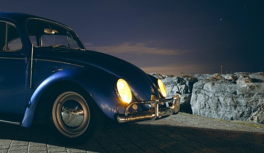 Fusca clássico à noite com os dois faróis acesos iluminando o calçamento